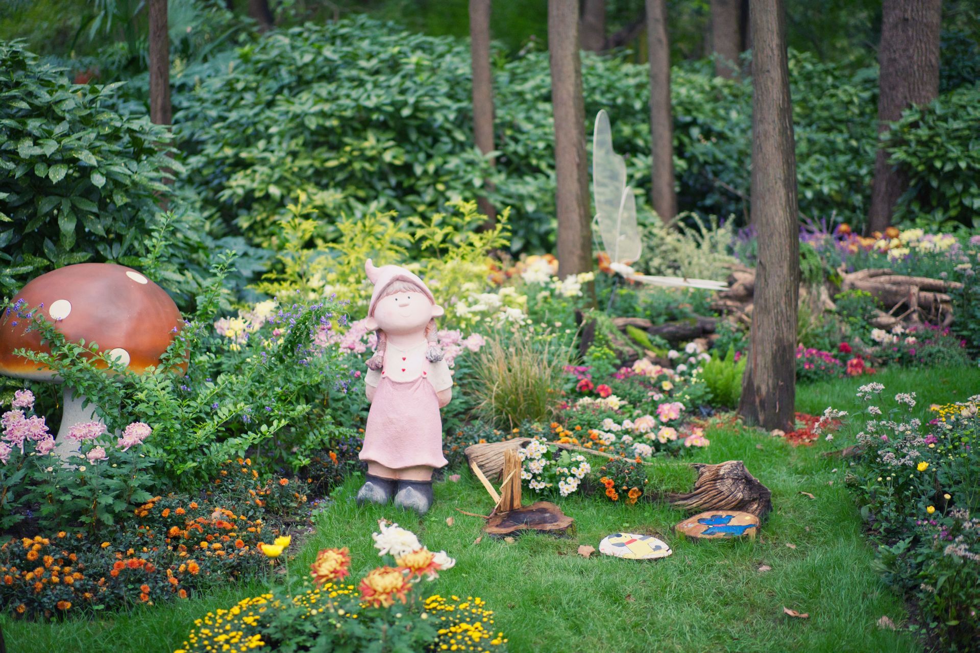 Garden with flowers and mushrooms, featuring a small pink statue amid lush greenery and trees