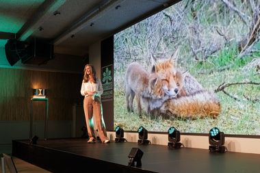 Een vrouw staat op het podium en presenteert op een scherm twee vossen 