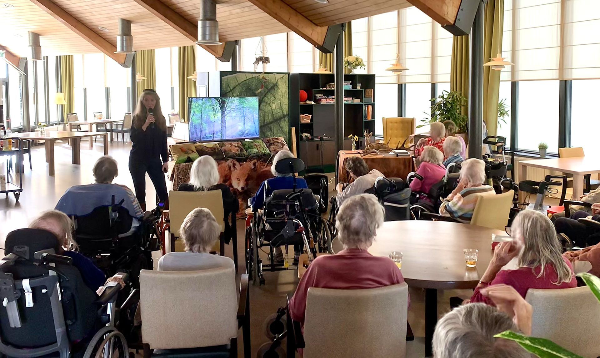 Vrouw geeft een presentatie over paddenstoelen aan een publiek; geprojecteerd beeld van paddenstoelen.