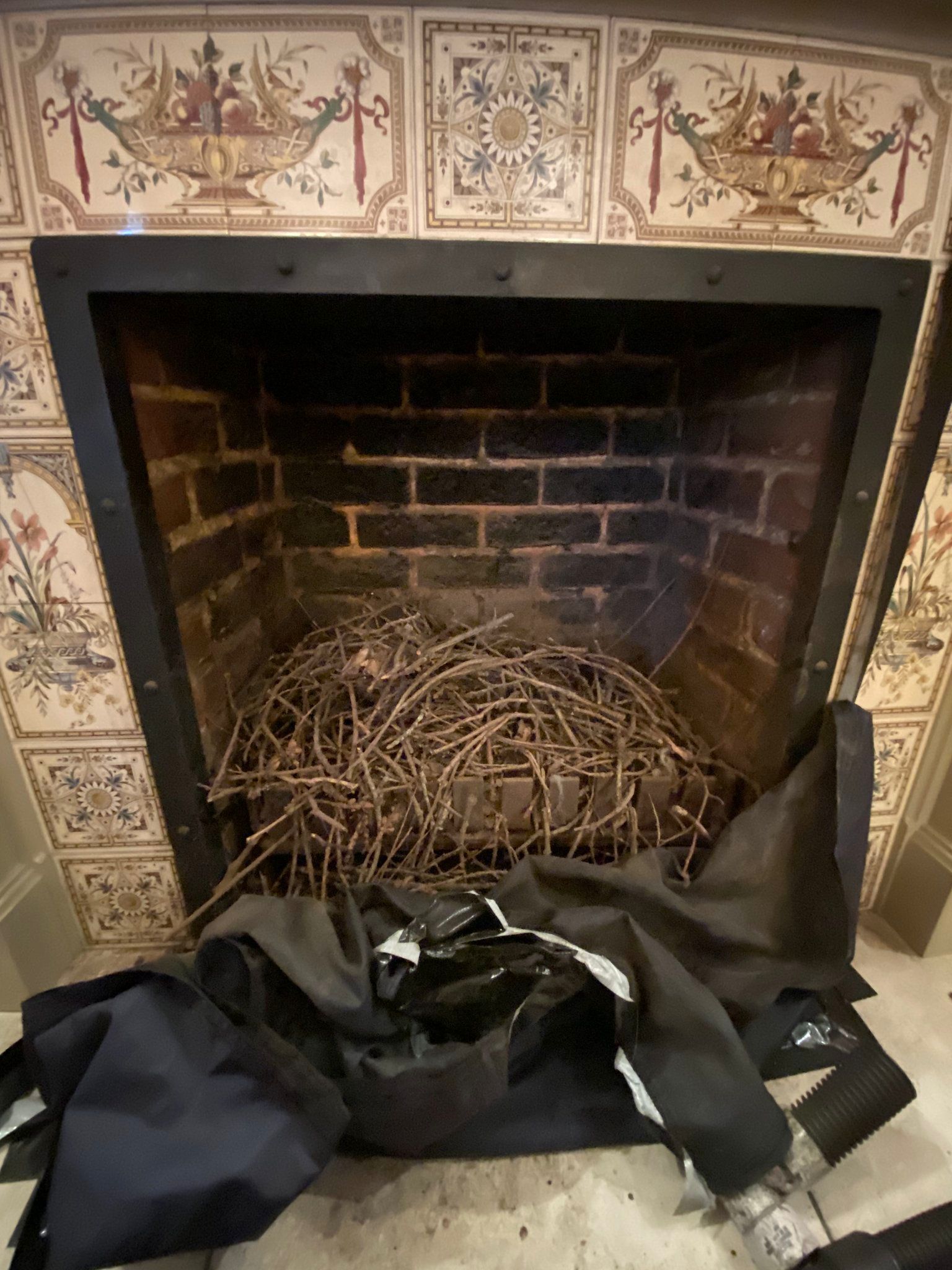 A fireplace filled with a large bird nest and a black tarp in front. Decorative tiles surround the brick fireplace.
