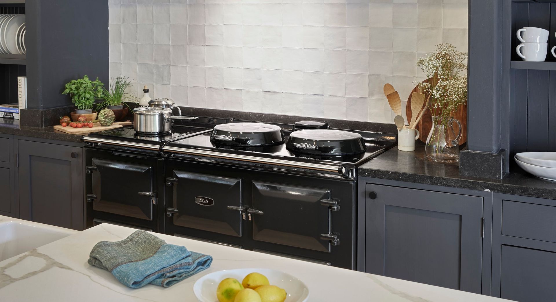 Black range cooker in a navy kitchen with white backsplash and countertop. A plate of lemons and towel are on the counter.