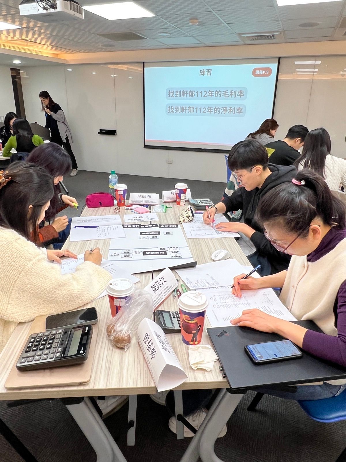 教室裡學員低頭寫筆記,投影幕上是課程實作題