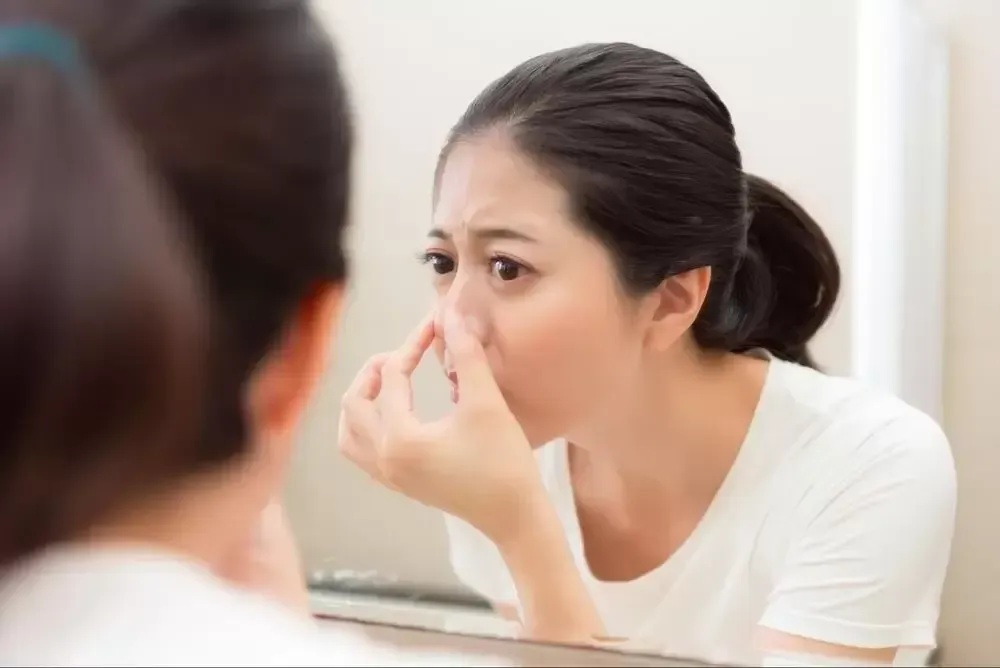 Woman looking in mirror, touching her nose, with concerned expression.