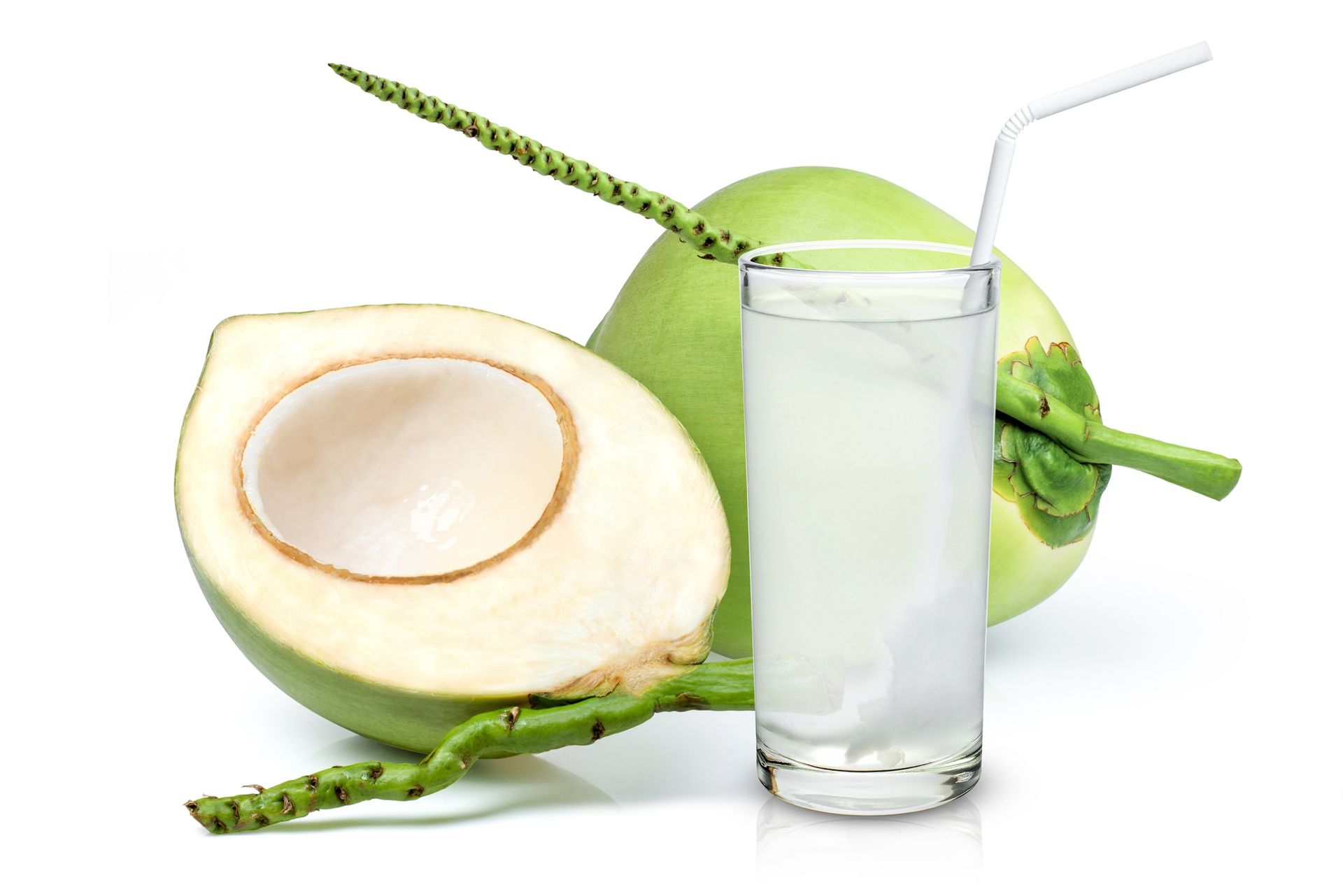 Green coconuts with a glass of coconut water and a straw. One coconut is cut open.