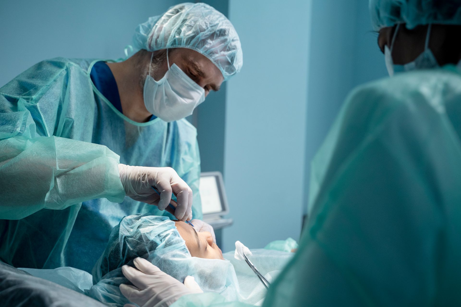 Surgeons in scrubs operate on a patient's face in a surgical room.
