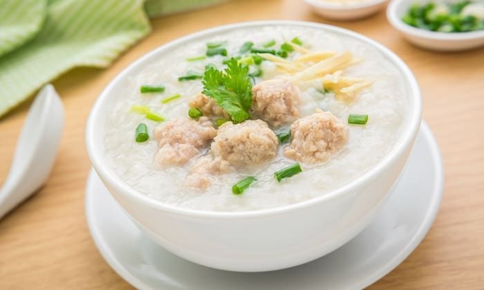 White bowl of congee topped with meatballs, green onions, and ginger.