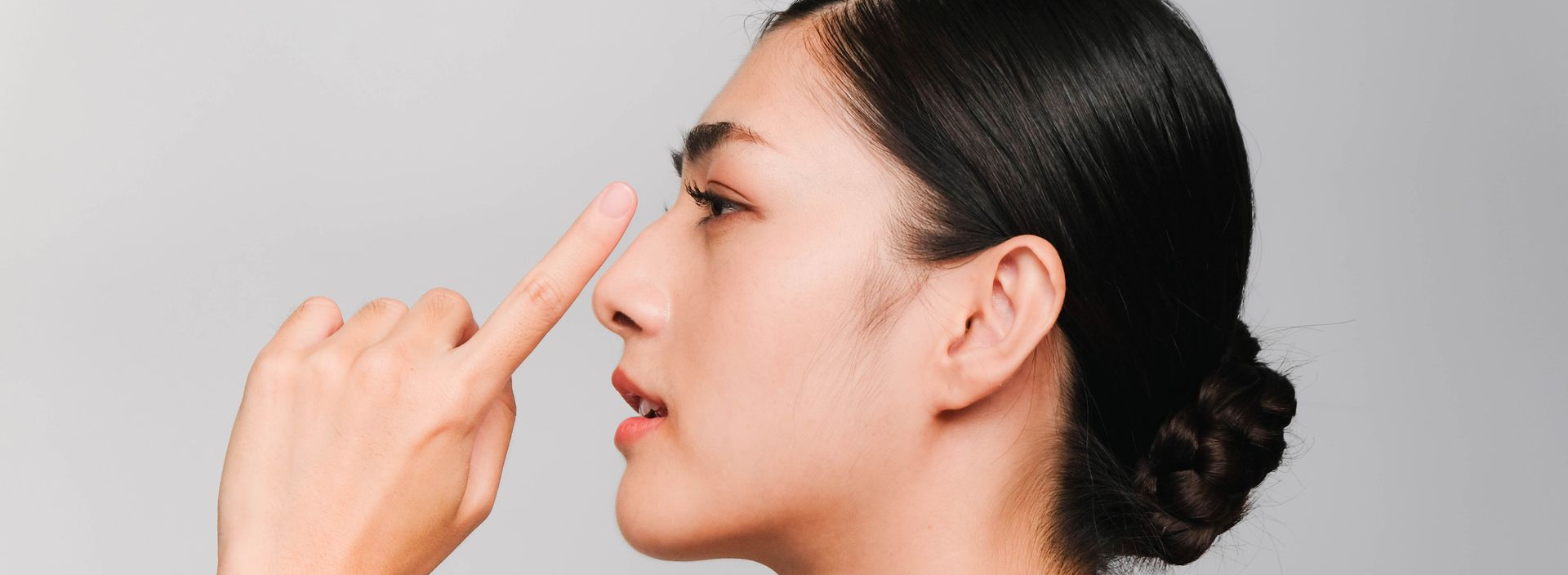 Woman touching her nose with her finger, profile view. Gray background.