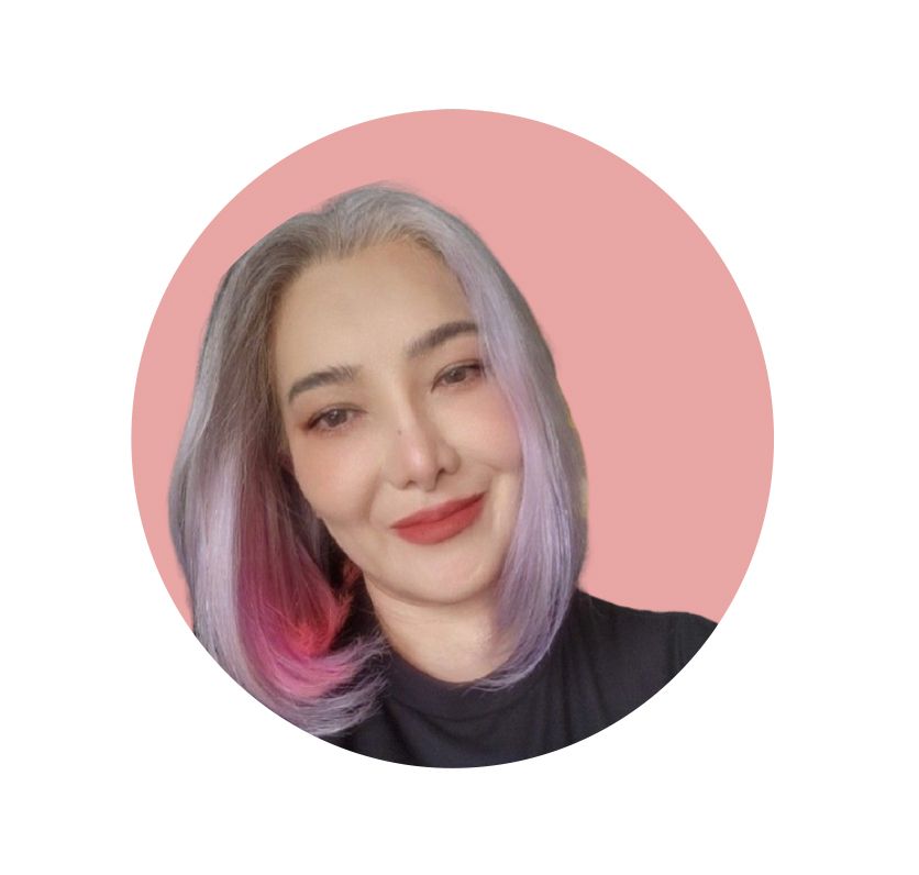 Woman with gray and pink hair, smiling, in a pink circle, wearing a black top.