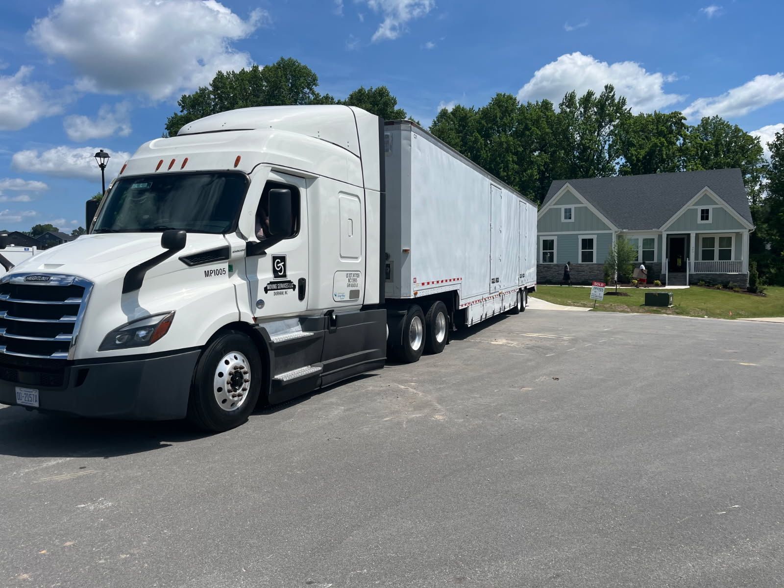 White semi-truck with trailer parked in a driveway beside a suburban house on a sunny day