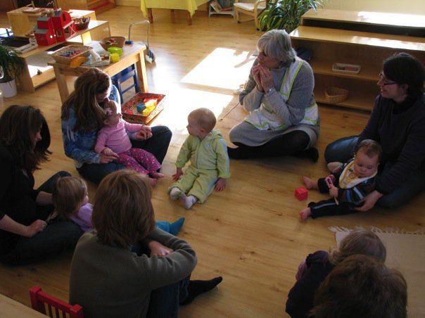 Montessori guides and babies sitting in a circle on a wooden floor, possibly a class or group session.