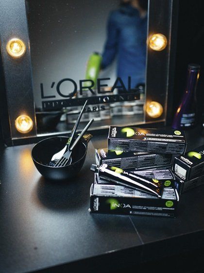 Haarverfproducten en -tools op een kaptafel. L'Oréal-spiegel met een persoon op de achtergrond.
