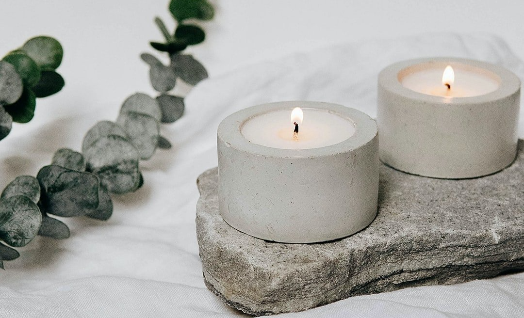 two candles are sitting on a rock next to eucalyptus leaves .