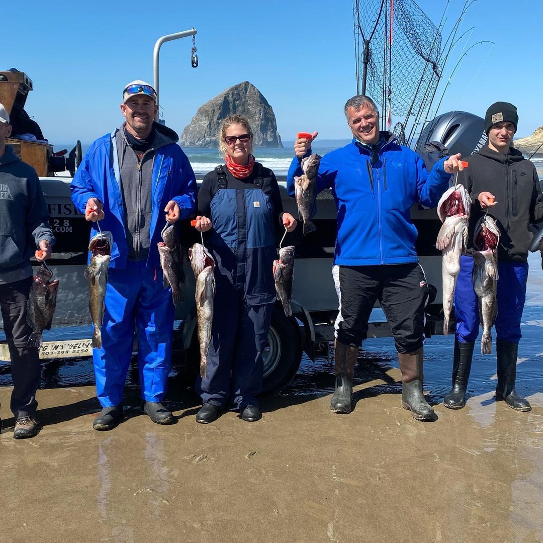 Group of people smiling, holding fish, standing on a boat dock, with a rock formation in the background.