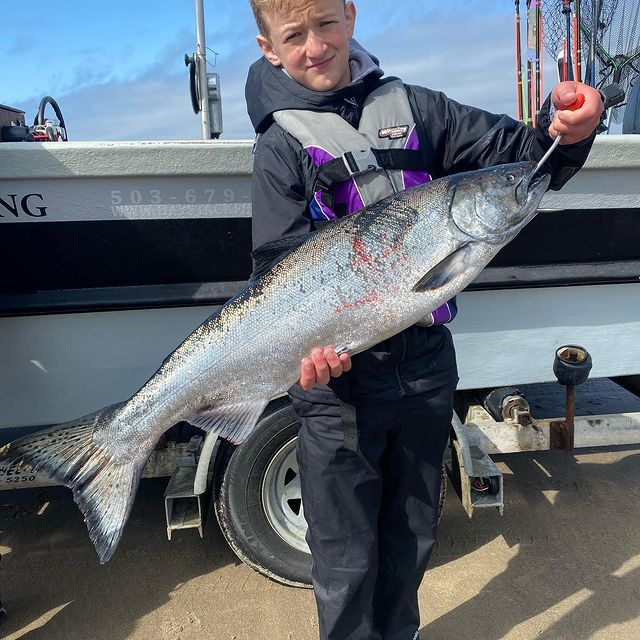 Young person holding a large silver salmon they caught on a boat in the outdoors.