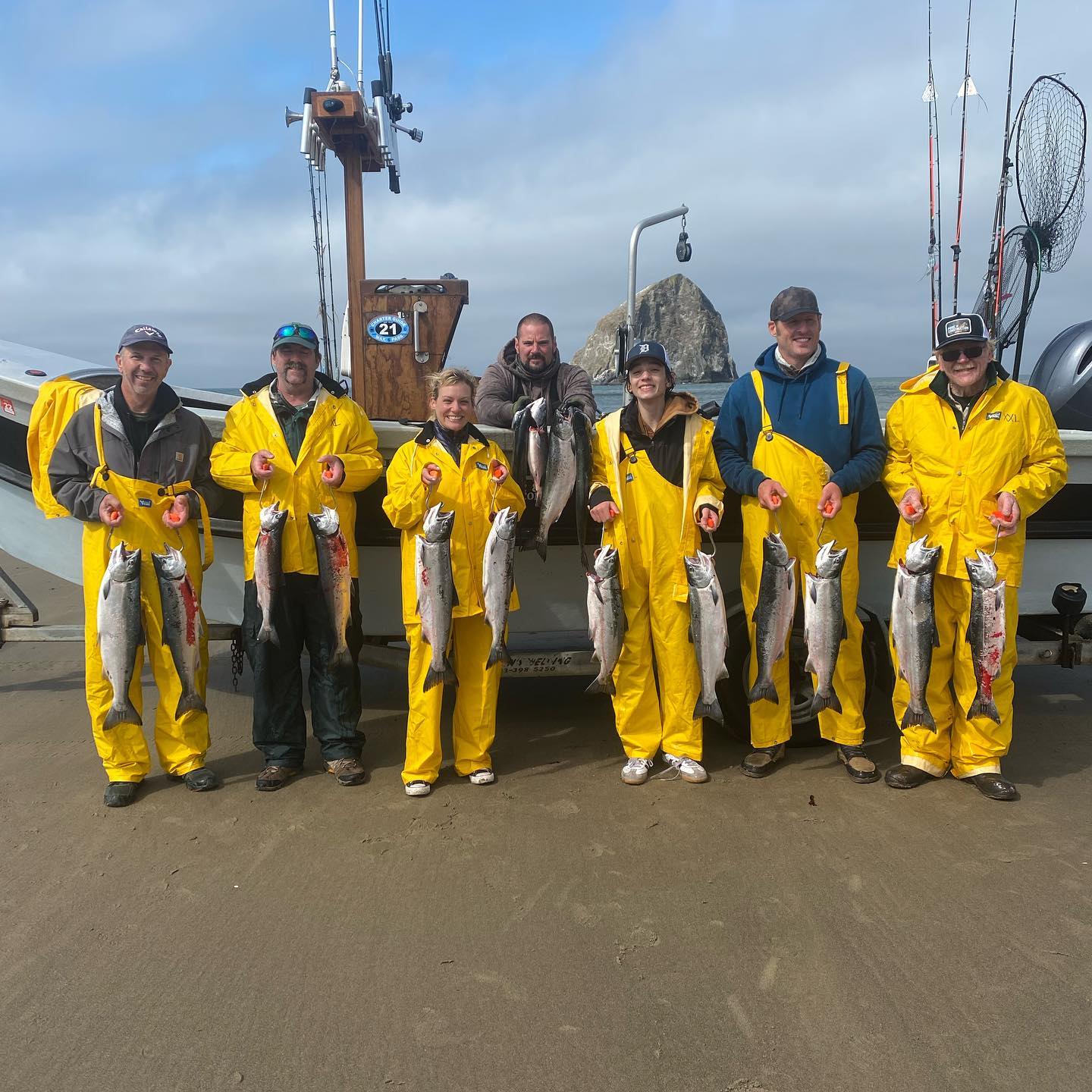 Group of people in yellow rain gear holding fish on a dock in front of a boat.