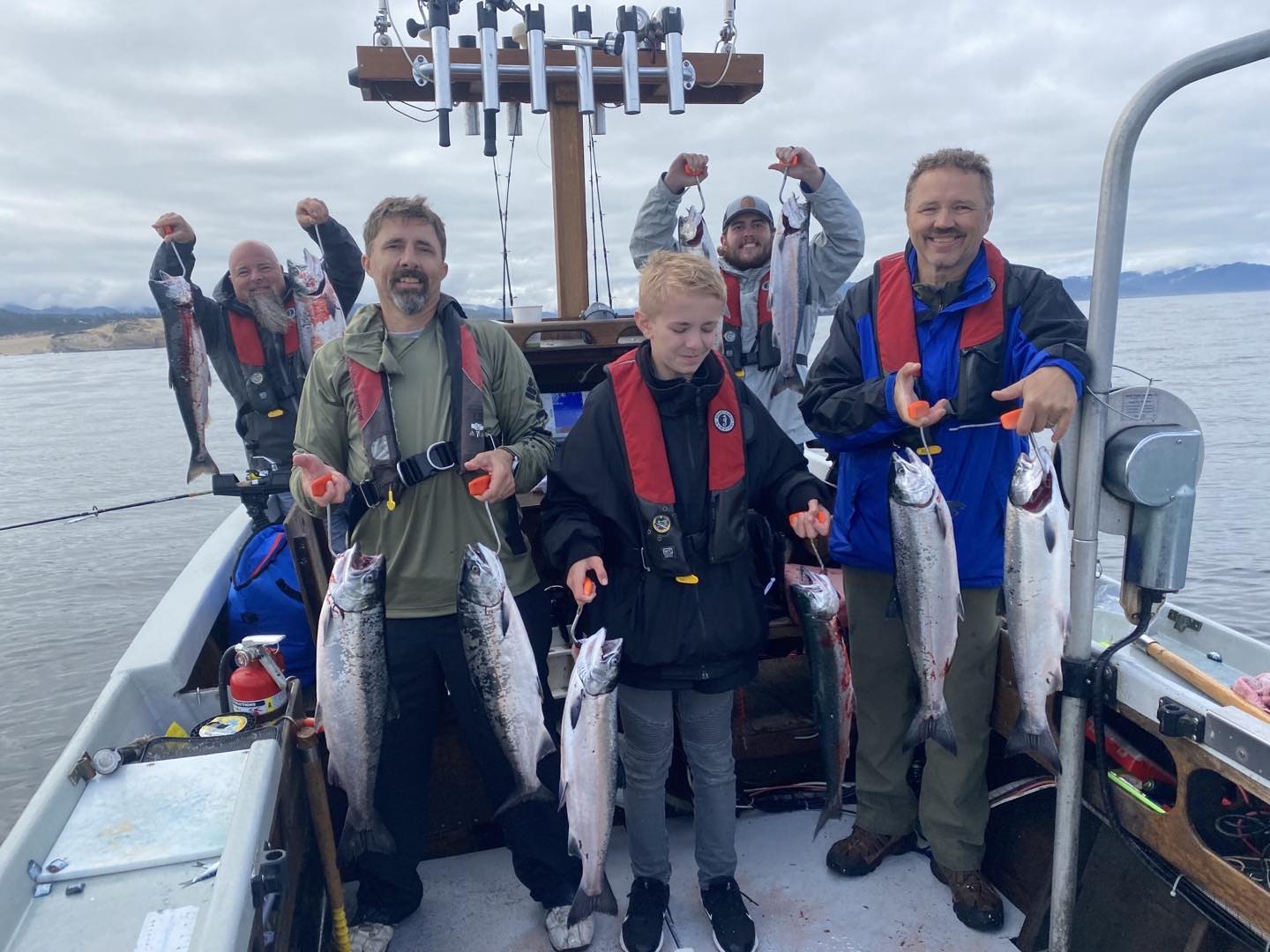 Group of people on a boat holding up fish they caught, smiling, in the ocean.