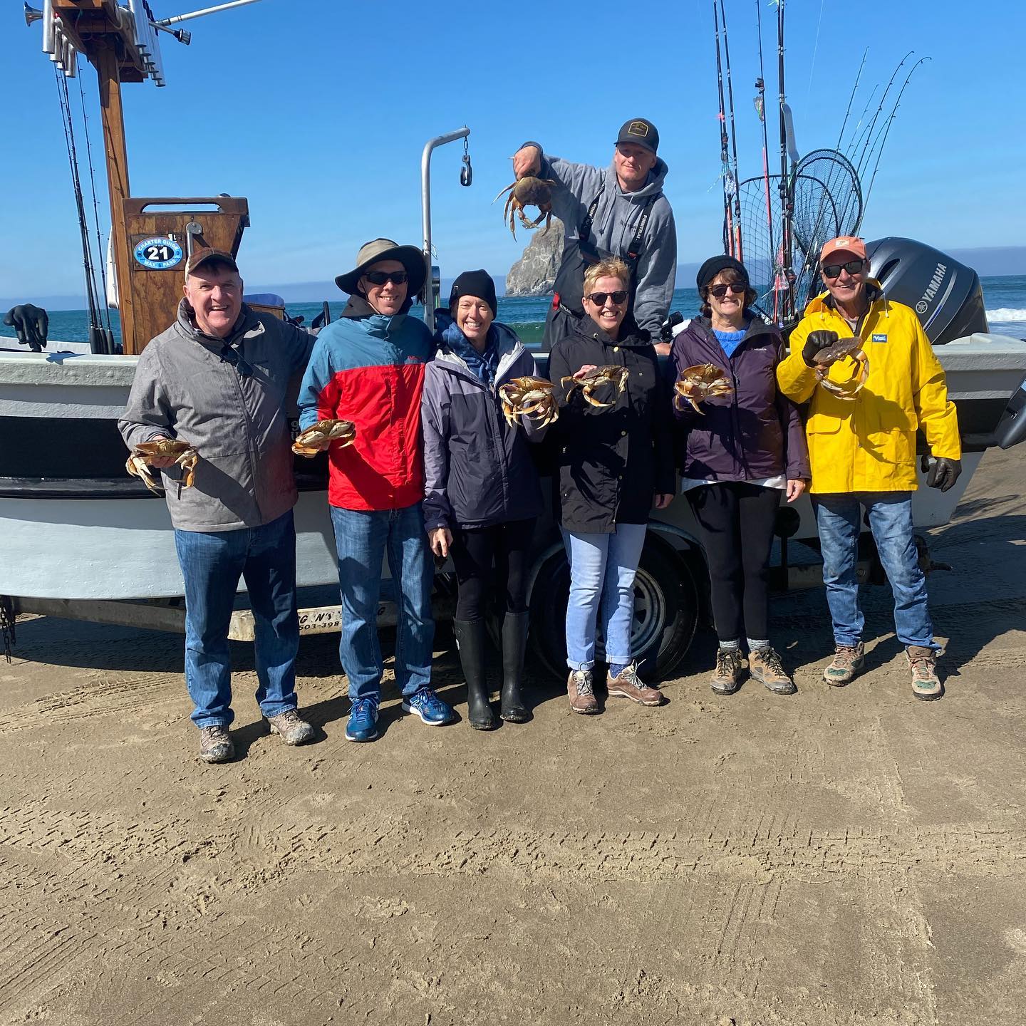Group of people holding crab, posing with a boat on a beach on a sunny day.