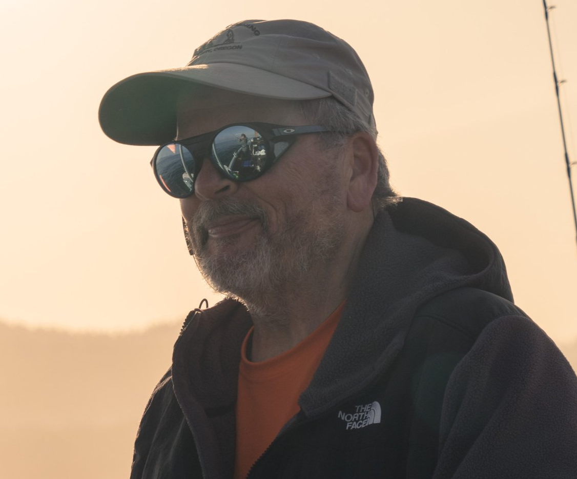 Man wearing hat and sunglasses, smiling, outdoors in soft sunlight.