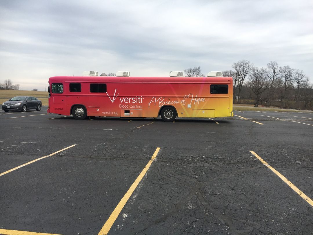 A red and yellow Versiti blood drive bus is parked in the church parking lot.