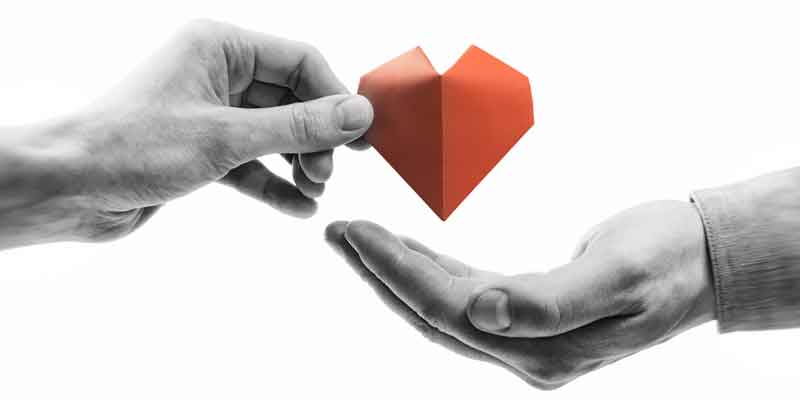 A person is giving a red paper heart to another person.