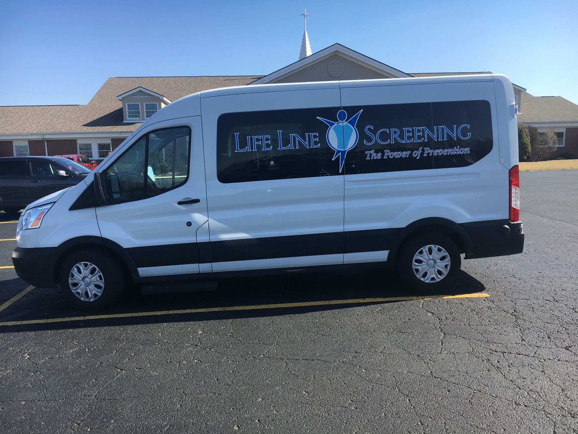 A white van is parked in a parking lot in front of Hanfield church. Lifescreening.
