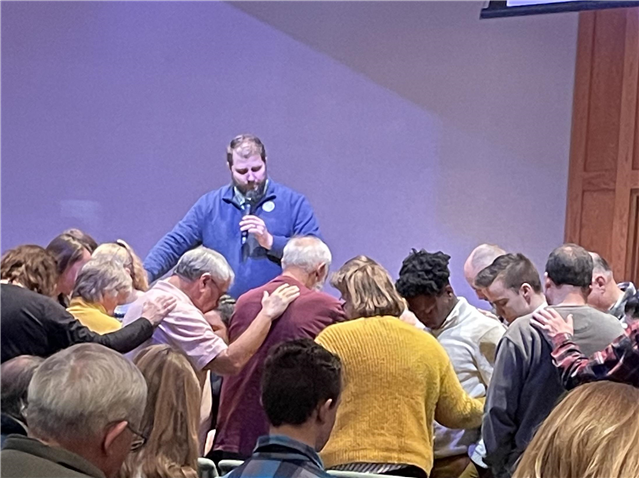 A group of people are praying in a circle with Pastor Derek.