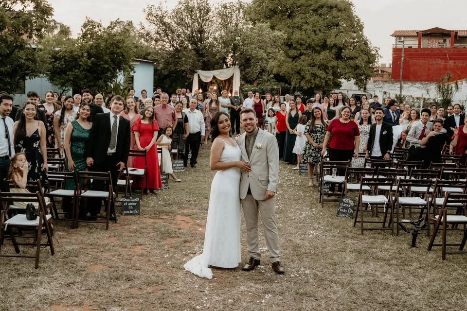 A bride and groom are Gabe and Dahiana Ernst posing for a picture in front of their wedding guests.