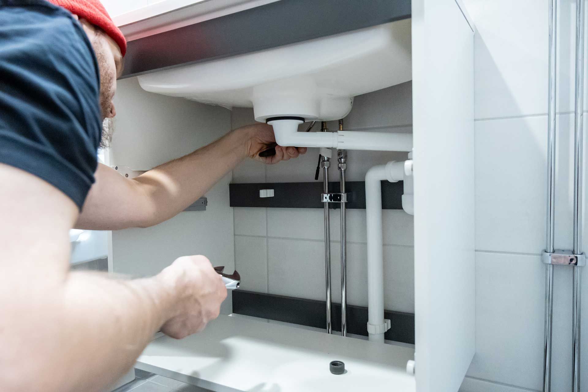 Person installing plumbing under a white sink cabinet