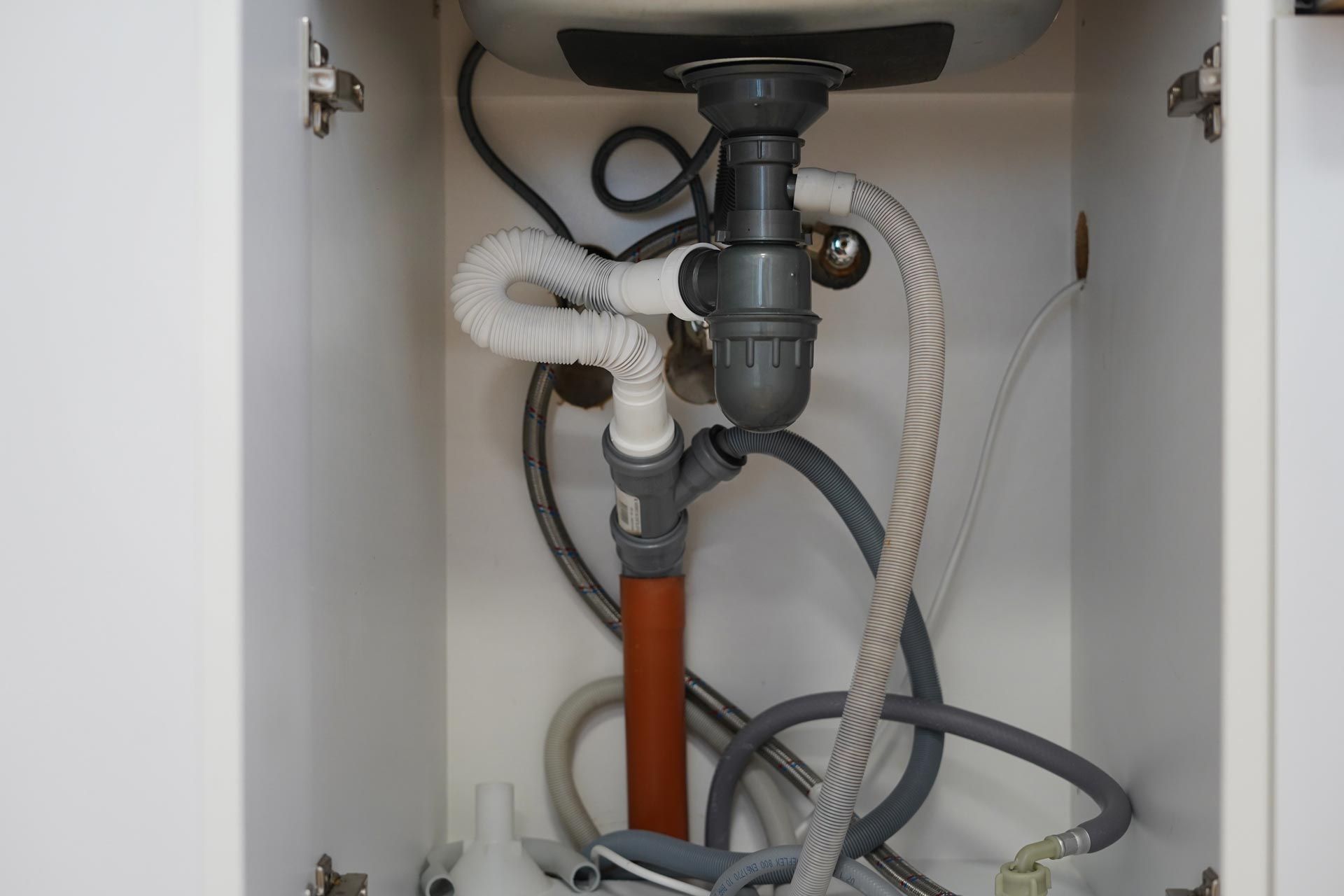 Under-sink plumbing with drain, pipes, and hoses inside a white cabinet