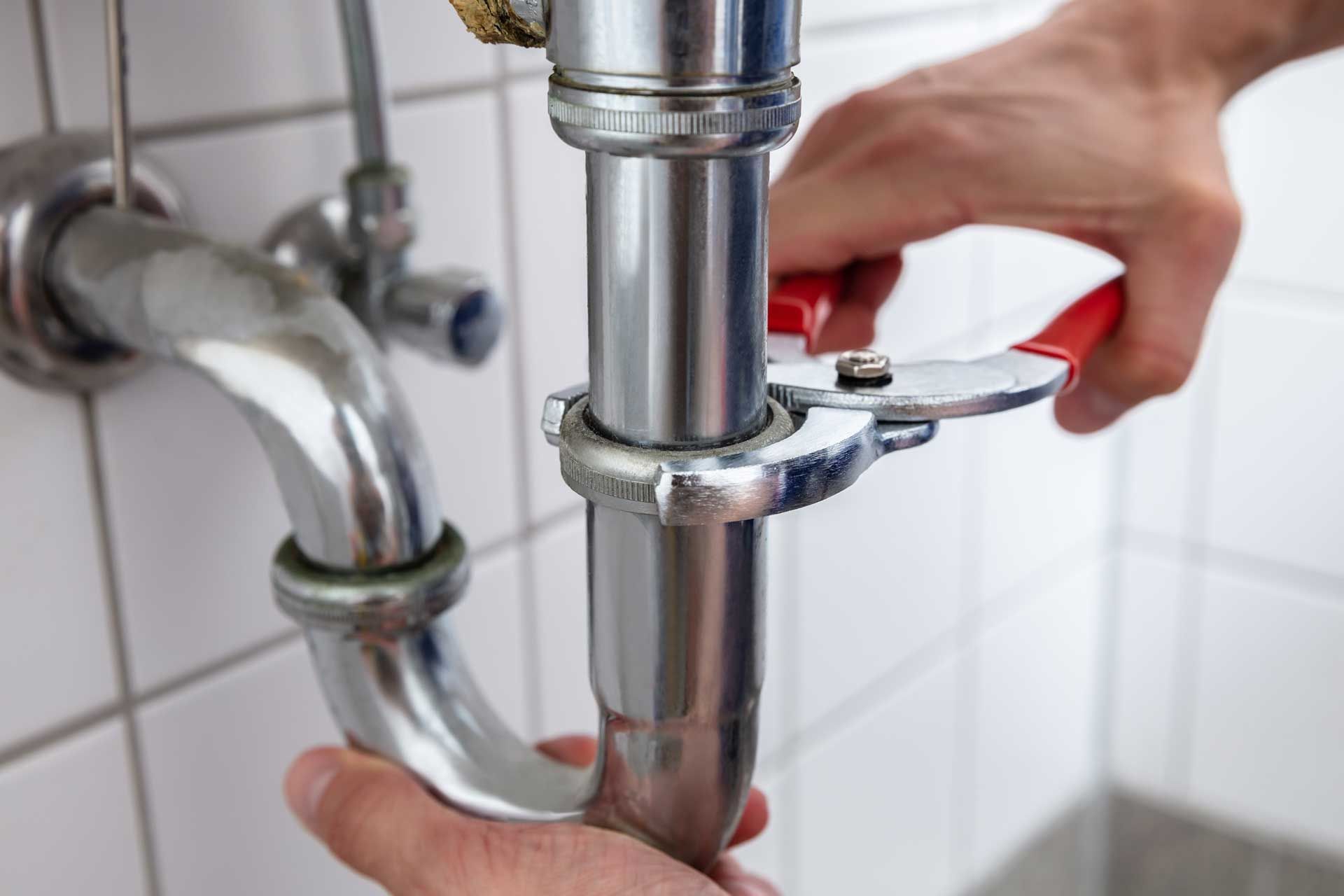 Hands using a wrench to tighten a chrome pipe under a sink