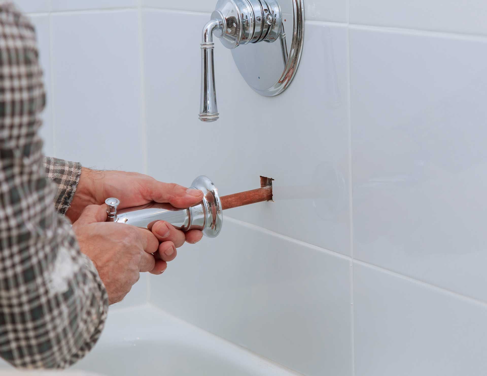 Hands installing a chrome shower fixture into a tiled bathroom wall with a wrench