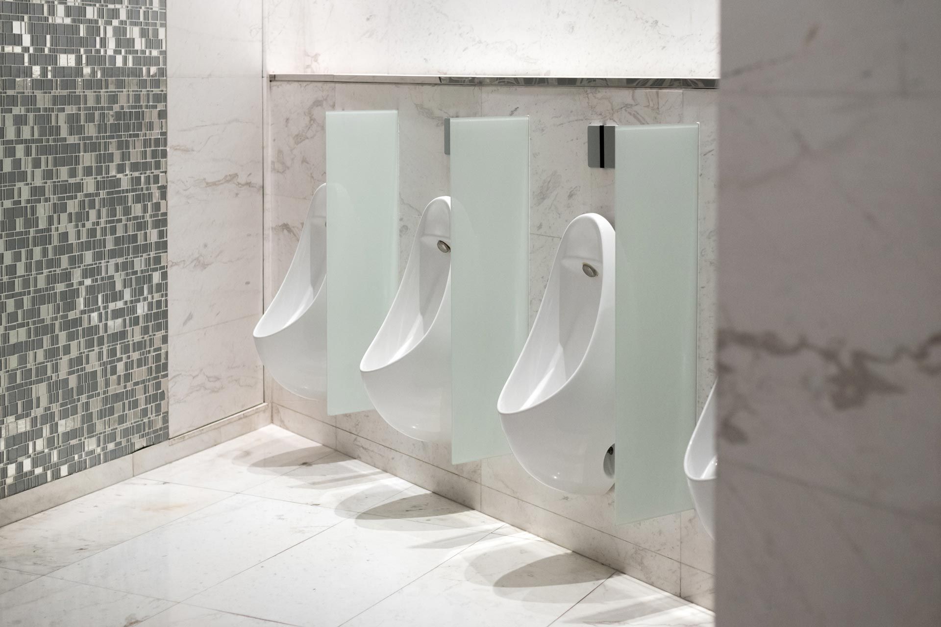 Row of white wall-mounted urinals in a clean, tiled public restroom