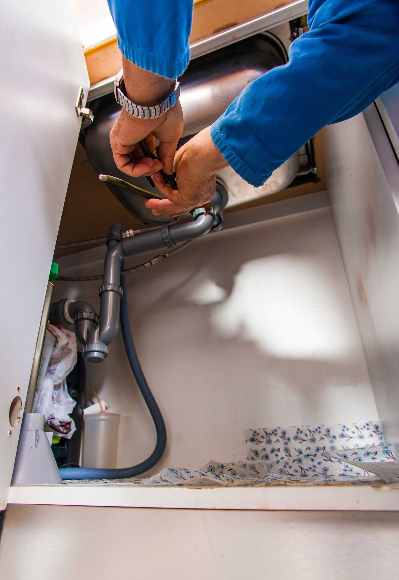 Hands connecting plumbing under a sink, with exposed pipes and a white cabinet interior.