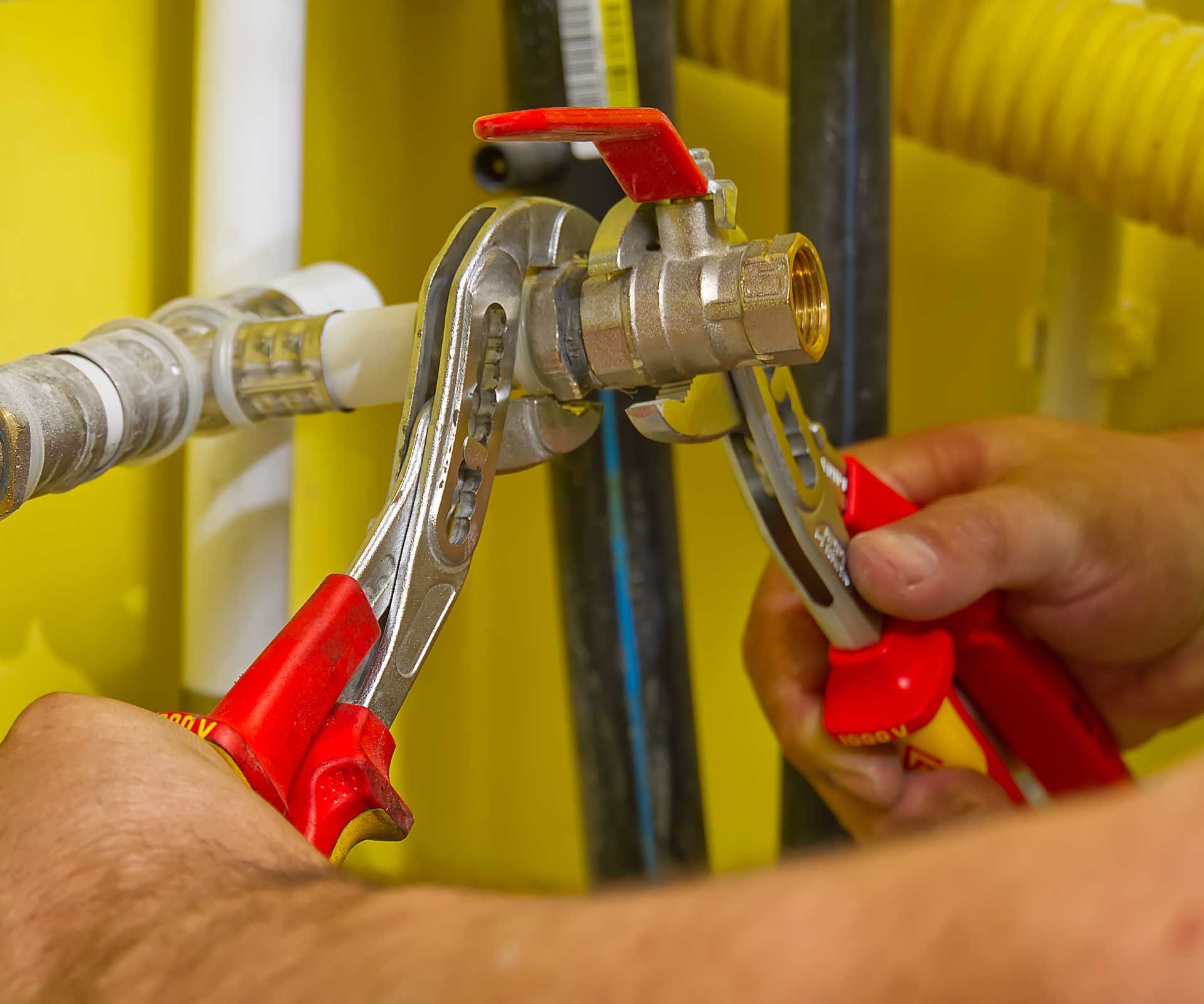 Hands using pliers to work on a metal pipe valve with a red handle.