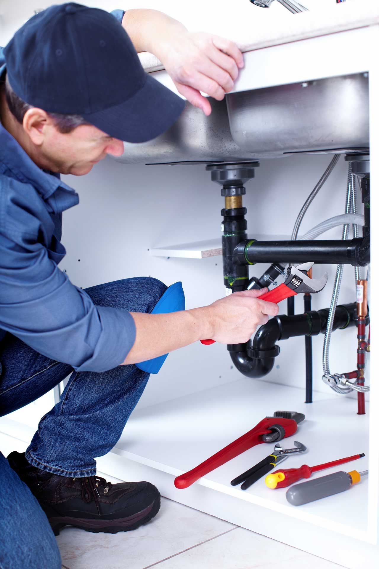 Plumber repairing a sink drain under a bathroom vanity with tools nearby