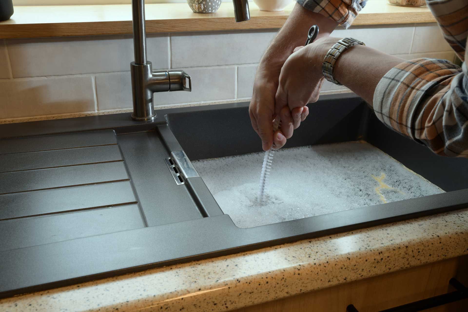 Hands washing in a stainless steel kitchen sink under a faucet, with soap suds in the basin.