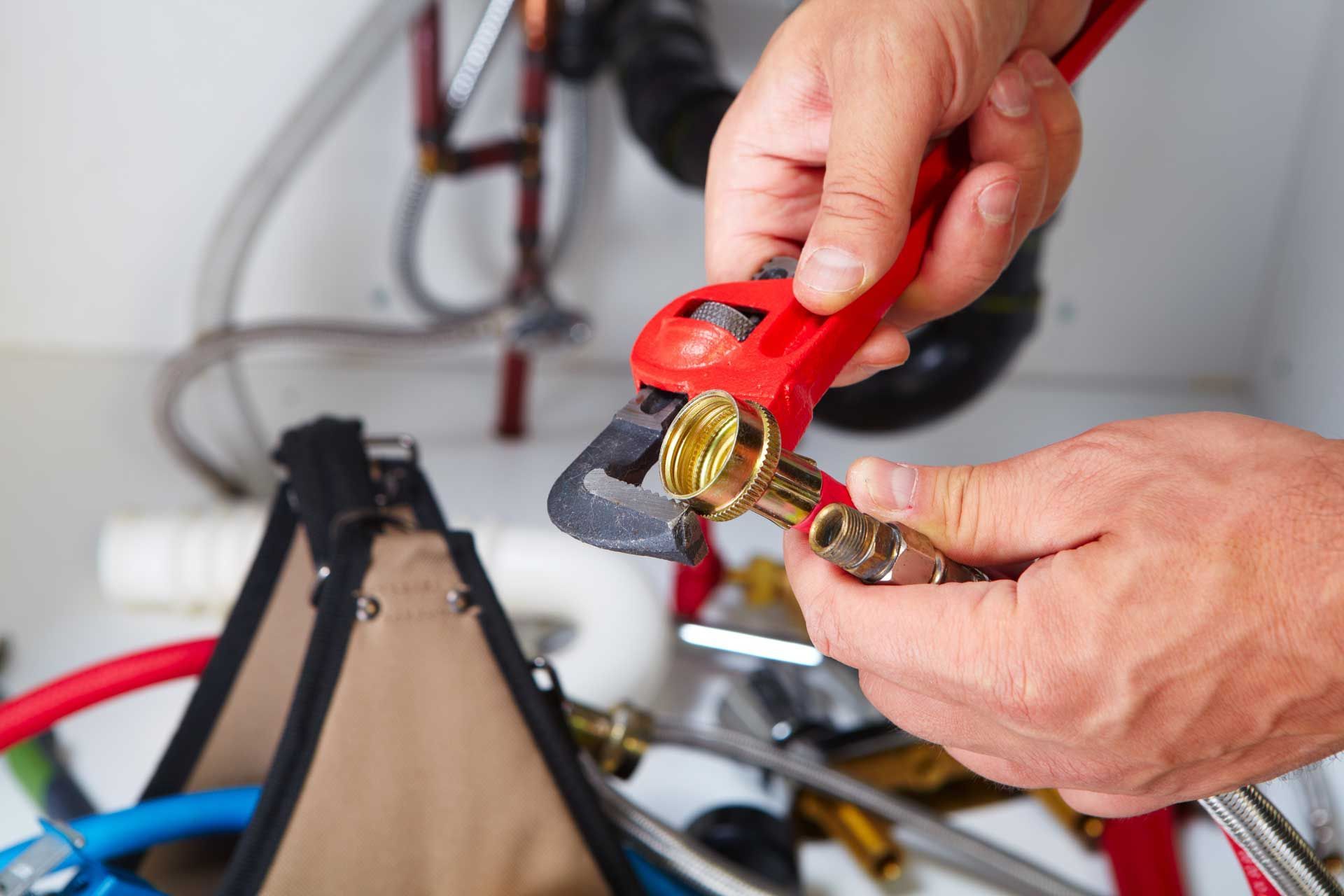 Hands using red pliers to cut a brass lock on a bicycle cable in a garage.