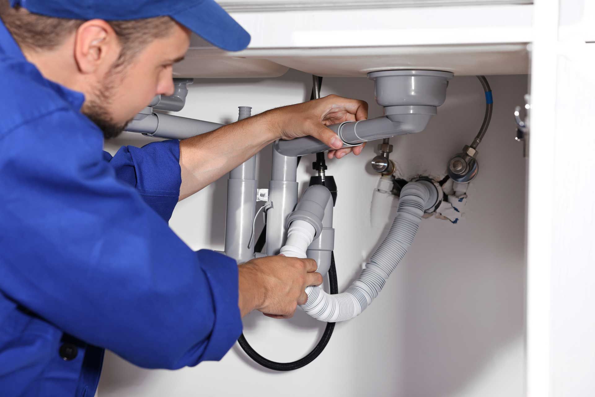 Plumber in blue uniform repairing pipes under a sink with a wrench