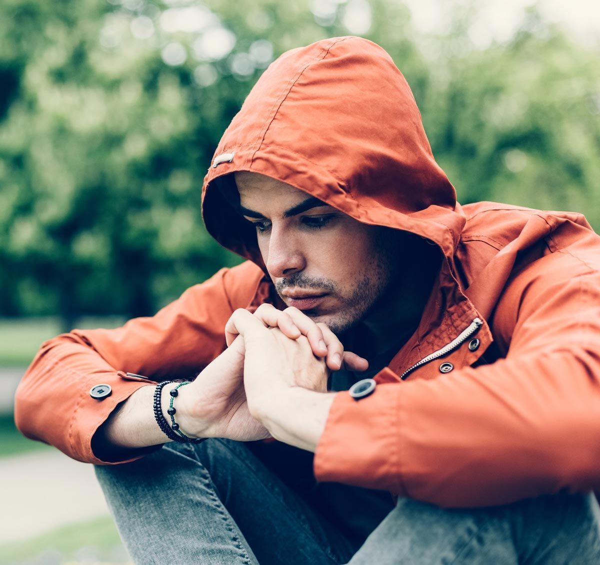 Man in orange jacket looking down with hands clasped feeling discouraged due to his marriage