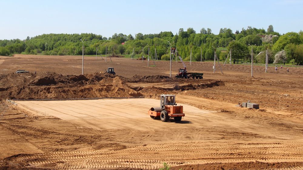 A Construction Site With an Orange Roller Compacting Soil — Northern Heavy Machinery in Townsville, QLD