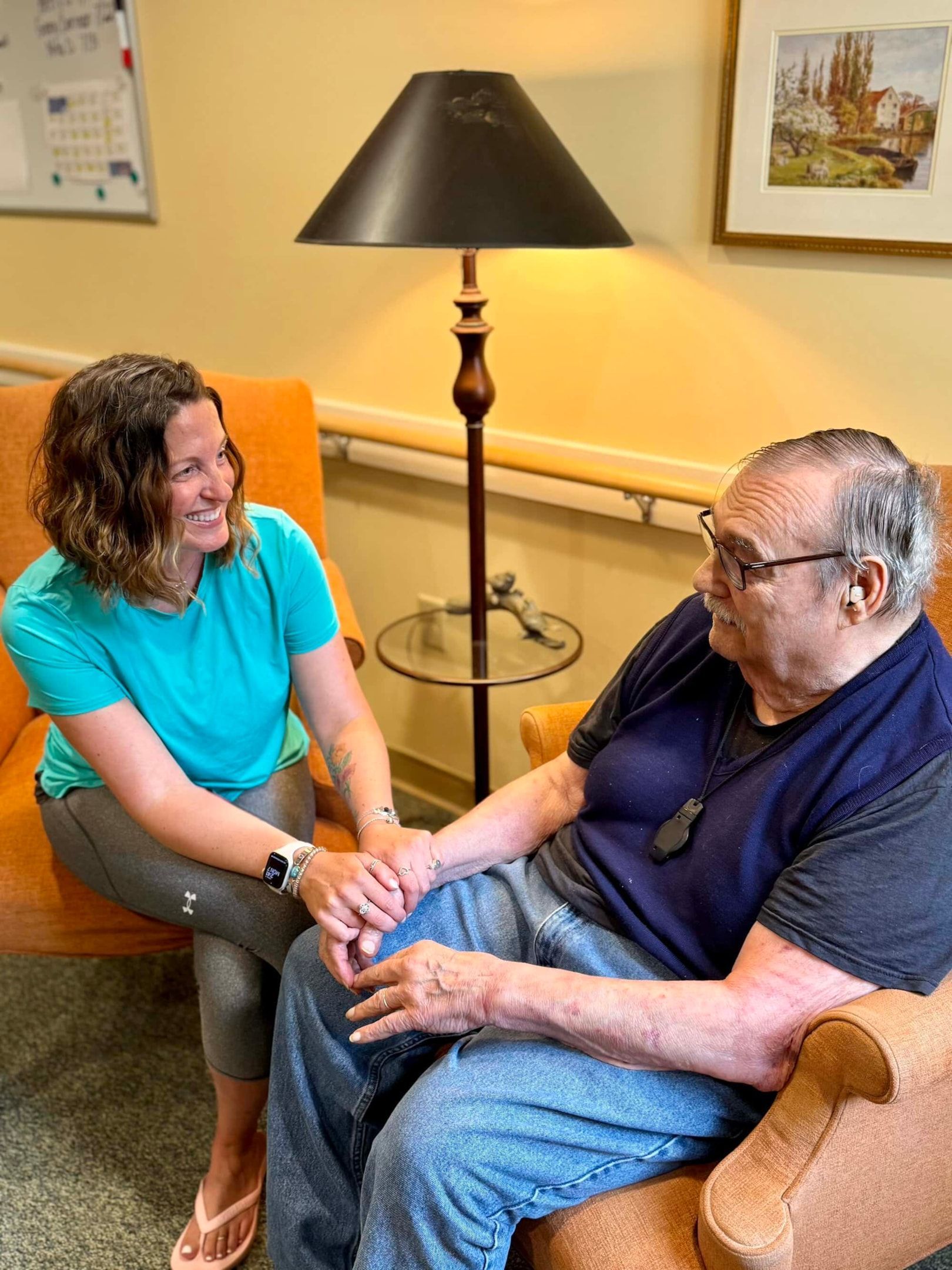 A child and an older adult laugh while facing each other, seated together in a sunlit room.