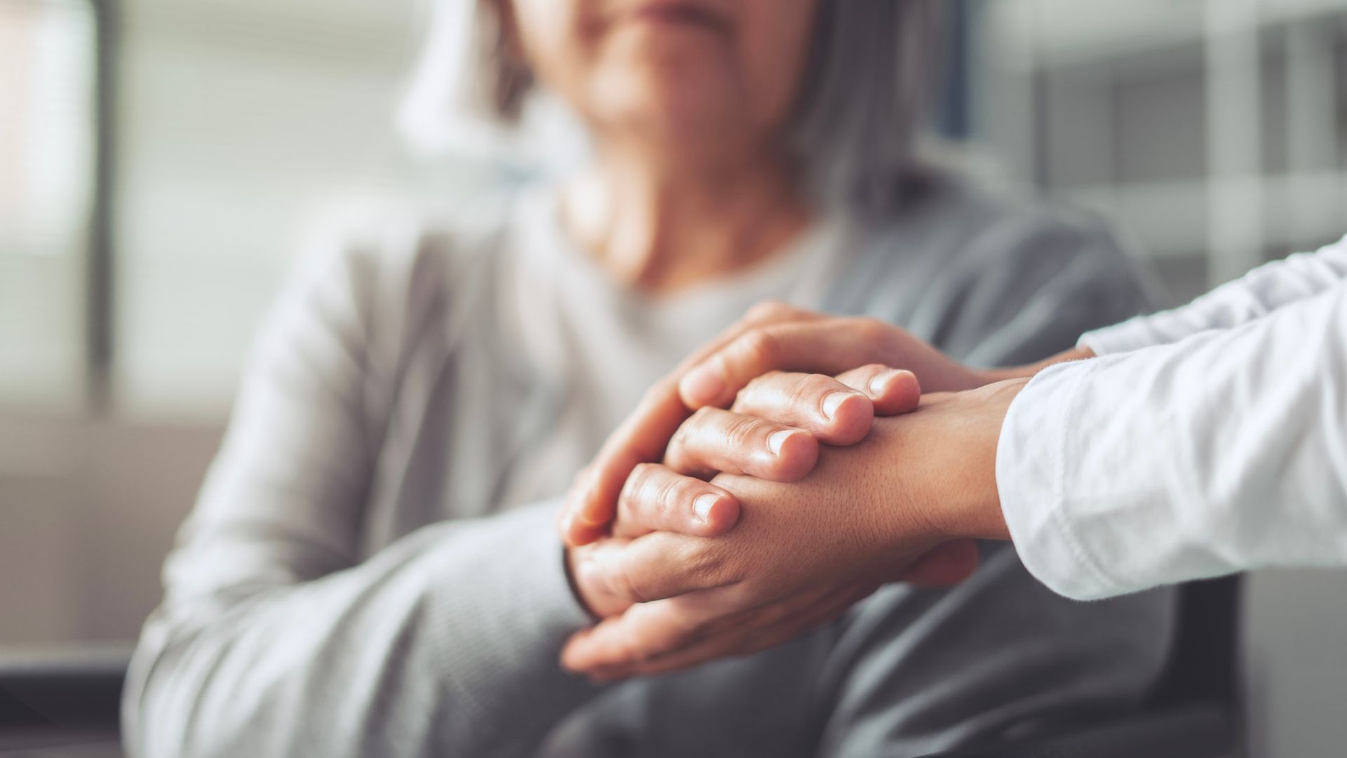 Hands clasped in support; one person comforts another with a gentle touch.