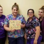 Four women in scrubs hold a sign saying,