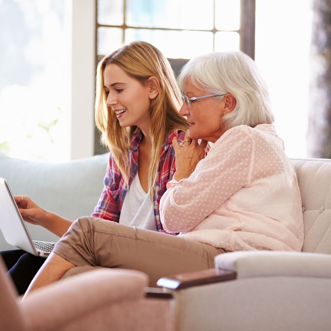 Woman and older adult looking at a laptop together on a couch.
