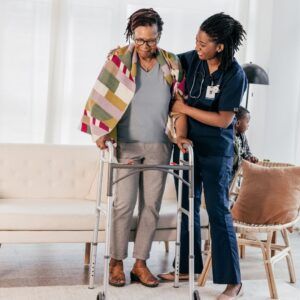 Caregiver assists person with walker in a living room.