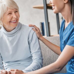 Smiling woman with caregiver, who is touching her shoulder, indoors.