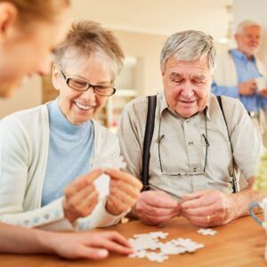 Two older adults and a younger person assemble a jigsaw puzzle indoors.
