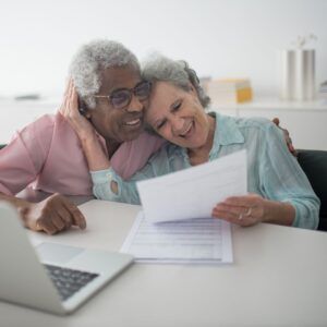 Couple at table, looking at paper and laughing, near a laptop.