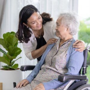 Woman with arm around an elderly person in a wheelchair, indoors.