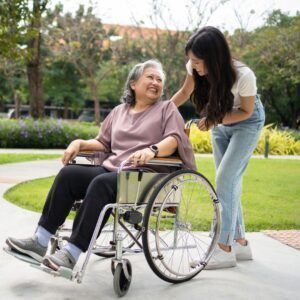 Woman in wheelchair smiling at person helping her outdoors.